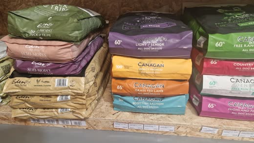 Stack of premium dry pet food sacks in purple, orange, green and cream on a warehouse shelf